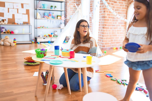 Bella insegnante e bambino sorridente pasti felici giocando con cibo di plastica e posate intorno a un sacco di giocattoli all'asilo
 - Foto, immagini