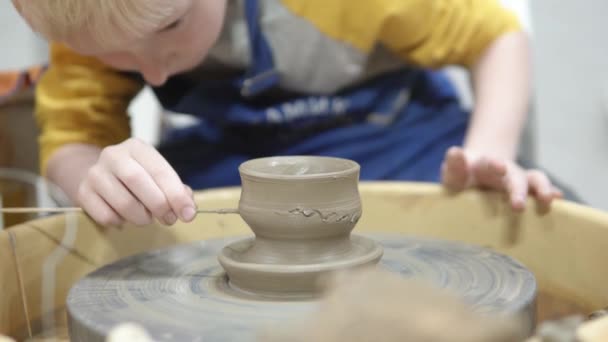 Jongen blond maakt een kopje klei op een pottenbakkerscirkel - Video