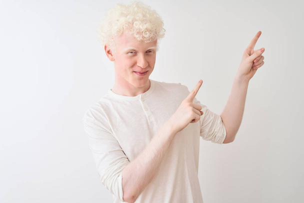 Young albino blond man wearing casual t-shirt standing over isolated white background smiling and looking at the camera pointing with two hands and fingers to the side. - Foto, imagen