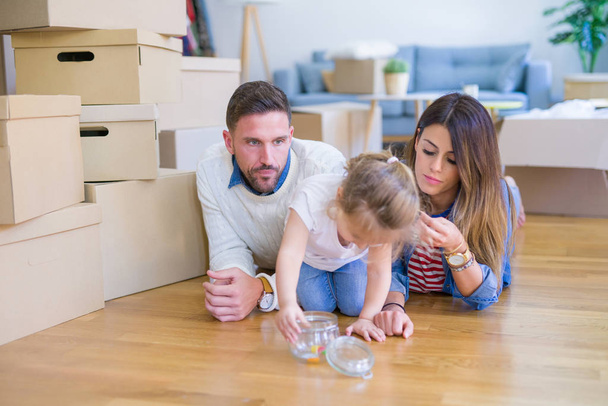 Bella famiglia con bambino sdraiato in una nuova casa intorno a scatole di cartone
 - Foto, immagini