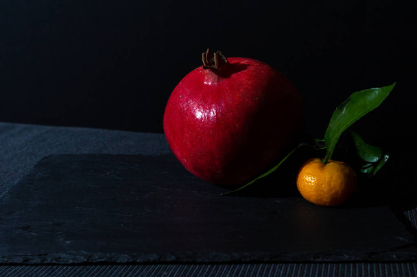 stilleven met granaatappel en mandarijn in een donkere sleutel. Samenstelling van vruchten op zwarte achtergrond. Ingrediënten voor vers sap. - Foto, afbeelding