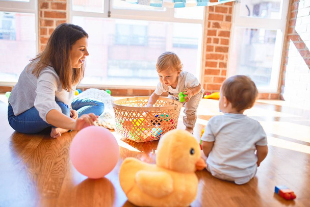 Beautiful teacher and toddlers playing around lots of toys at kindergarten - Foto, Imagen