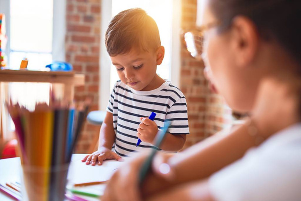 Mooie leraar en peuter jongen tekening tekenen met behulp van gekleurde potloden op de kleuterschool - Foto, afbeelding