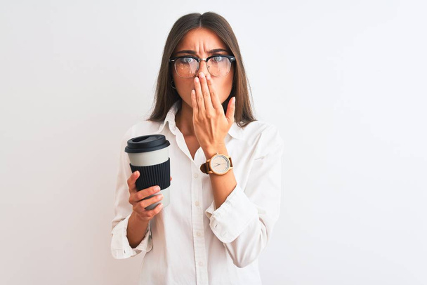 Jeune femme d'affaires portant des lunettes boire du café sur fond blanc isolé couvrir la bouche avec la main choquée par la honte pour erreur, expression de la peur, peur dans le silence, concept secret
 - Photo, image