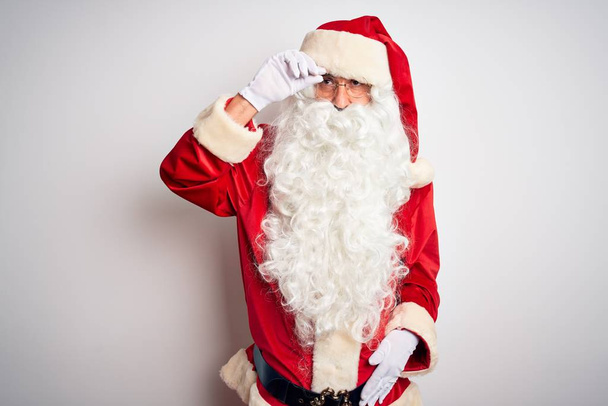 Ein gutaussehender Mann mittleren Alters im Weihnachtsmannkostüm steht vor isoliertem weißen Hintergrund und deutet unglücklich auf Pickel auf der Stirn, hässliche Mitesser-Infektion. Akne und Hautprobleme - Foto, Bild