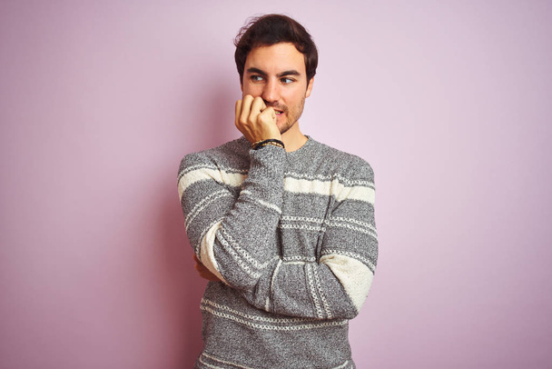 Jonge knappe man met casual gestreepte trui over geïsoleerde roze achtergrond kijkend gestresst en nerveus met handen op de mond bijtende nagels. Angst probleem. - Foto, afbeelding