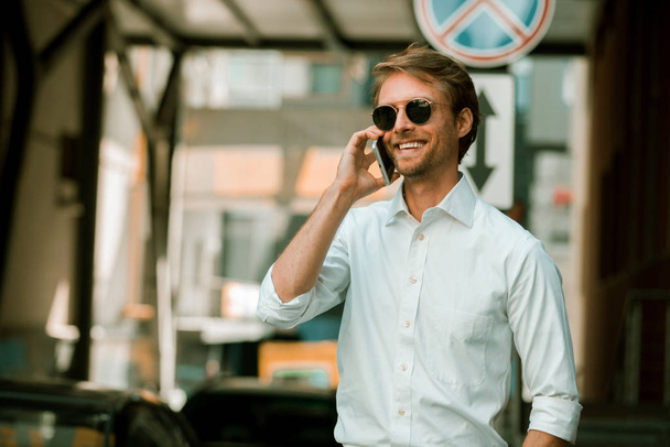 Ο επιχειρηματίας με τα γυαλιά ηλίου μιλώντας στο τηλέφωνο και χαμογελώντας - Φωτογραφία, εικόνα