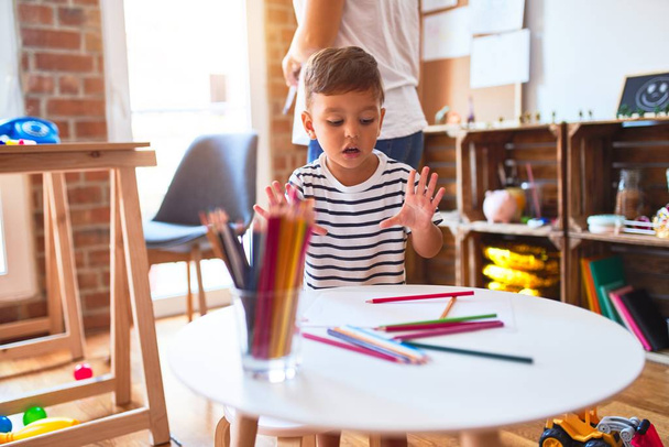 Kaunis opettaja ja lapsi poika piirustus piirtää käyttäen värillisiä kyniä päiväkodissa
 - Valokuva, kuva
