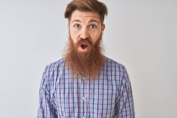 Redhead irish man listening to music using wireless earphones over isolated white background afraid and shocked with surprise expression, fear and excited face. - Photo, Image