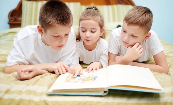 Tre bambini stanno esaminando solo un libro
 - Foto, immagini