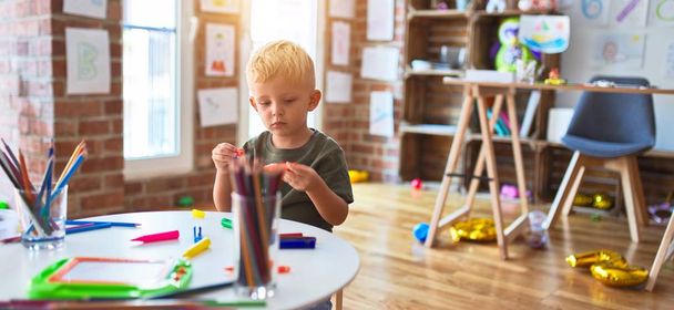 Young caucasian kid playing at kindergarten drawing with color pencils. Preschooler boy happy at playroom. - Фото, изображение