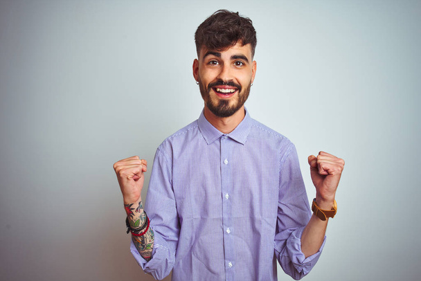 Fiatal férfi tetovált visel lila ing felett áll elszigetelt fehér háttér ünneplő meglepett és csodálkozott a siker karok felemelt és nyitott szemmel. Nyertes koncepció. - Fotó, kép