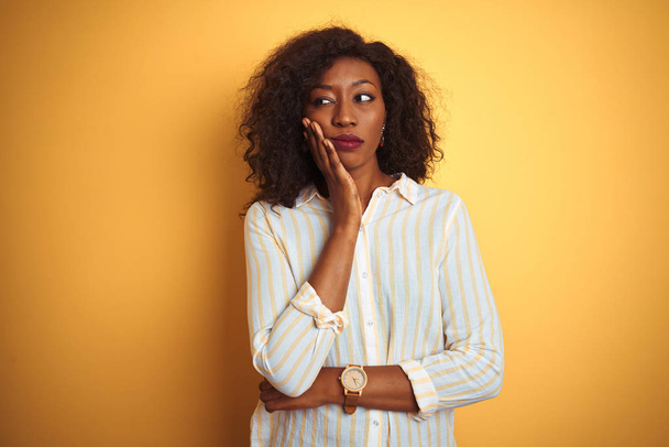 African american woman wearing striped shirt standing over isolated yellow background thinking looking tired and bored with depression problems with crossed arms. - Foto, imagen