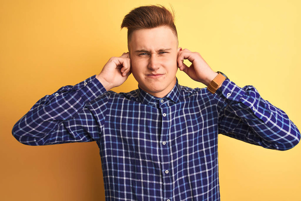 Young handsome man wearing casual shirt standing over isolated yellow background covering ears with fingers with annoyed expression for the noise of loud music. Deaf concept. - Photo, Image