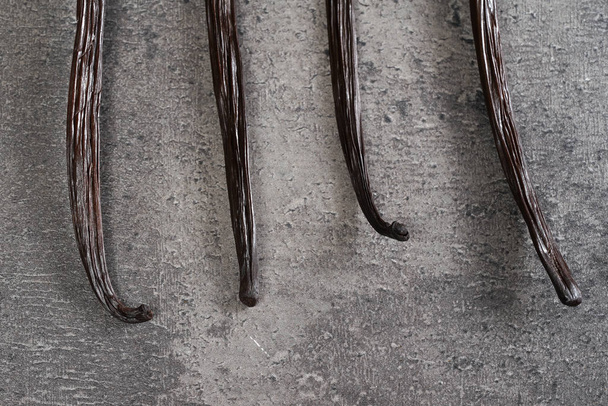 Four vanilla beans pods on gray kitchen table, close up detail from above - Valokuva, kuva