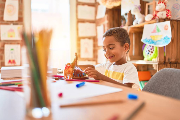 Beautiful african american toddler playing with dinosaurs toy on desk at kindergarten - Photo, image
