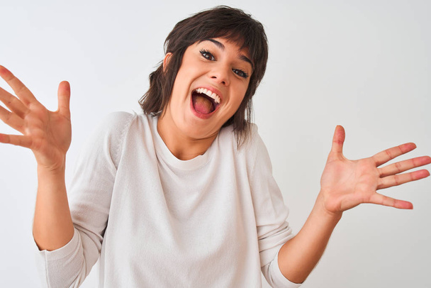 Young beautiful woman wearing casual t-shirt standing over isolated white background very happy and excited, winner expression celebrating victory screaming with big smile and raised hands - Photo, Image