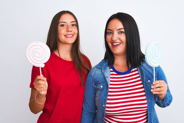 Young beautiful women holding sweet lollipop standing over isolated white background with a happy face standing and smiling with a confident smile showing teeth - Photo, Image