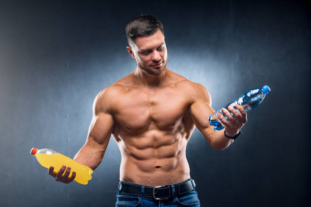 Sexy sportsman holding a bottle of water and soda. Choosing between healthy and harmful drink. Portrait. Closeup - Photo, Image