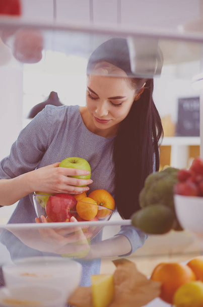Mosolygó nő vesz egy friss gyümölcsöt ki a hűtőből, egészséges étel koncepció - Fotó, kép