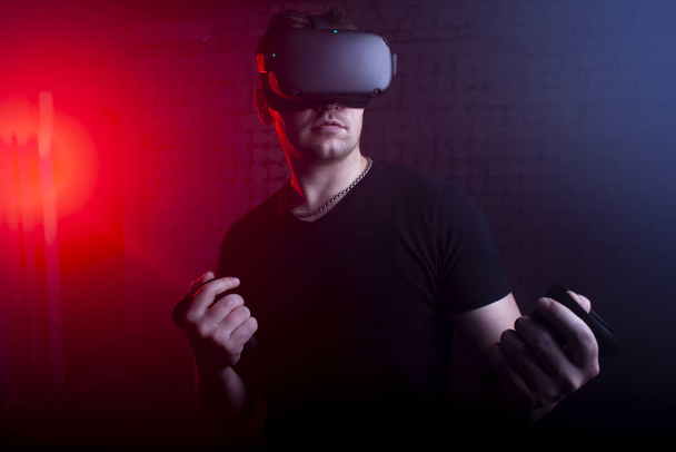 VRメガネを持つ深刻な残忍な男は、仮想現実の部屋に立っており、ジョイスティック、男性ゲーマー、仮想世界で再生 - 写真・画像