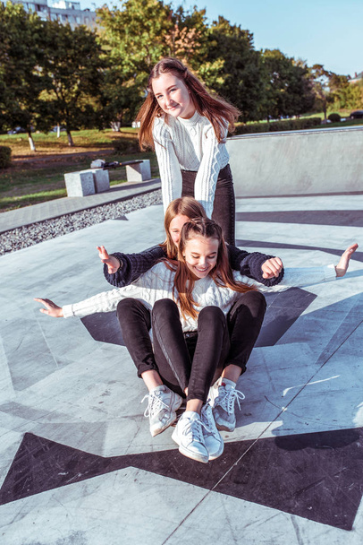 3人の女の子のガールフレンドのティーンエイジャー12-15歳、スケートボードに乗る、昼の街の通り、幸せな笑顔を楽しむ学校の大学の後に楽しみを持っています。感情リラクゼーションエンターテイメント、カジュアルウェアスニーカージーンズセーター - 写真・画像