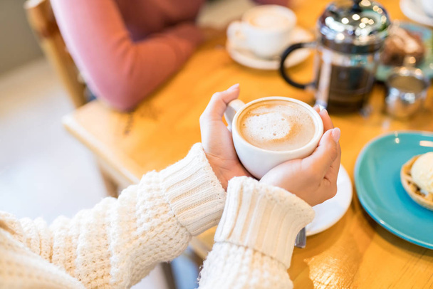 Midsection ženy drží šálek kávy, zatímco sedí s přítelem v kavárně - Fotografie, Obrázek