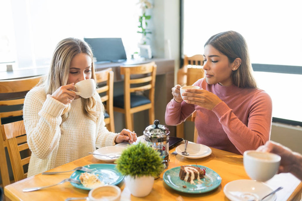 Друзья пьют кофе во время десерта за столом в кафе
 - Фото, изображение