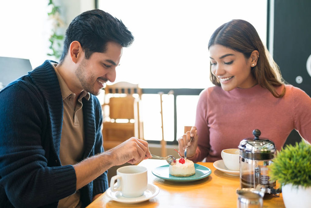 Smiling young couple sharing dessert at table in cafe - Фото, изображение