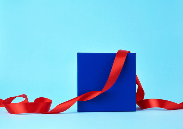 caja de cartón azul cuadrado para un regalo y cinta roja de seda retorcida
 - Foto, Imagen
