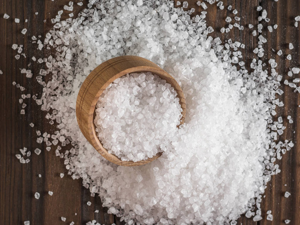 Vista superior de una gran cantidad de sal dispersa con una taza de madera
. - Foto, Imagen