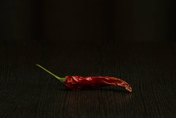 Вид сбоку, струйка сушеного красного перца чили на темном деревянном столе на черном фоне
. - Фото, изображение