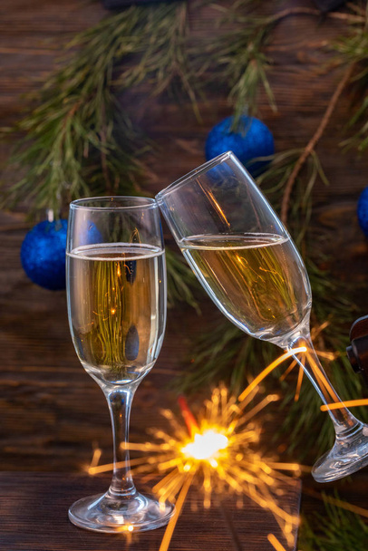 Glasses of champagne with bubbles on the background of Christmas decorations. Glasses touch during a festive toast and sparklers burn beautifully. Beautiful card. - Photo, Image