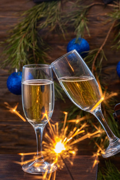 Lasit samppanjaa kuplia taustalla joulukoristeita. Lasit koskettavat juhlallisen paahtoleivän aikana ja sädehtijät palavat kauniisti. Kaunis kortti
. - Valokuva, kuva