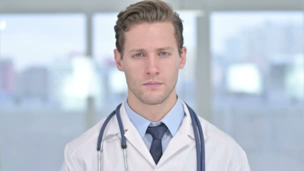 Porträt eines jungen männlichen Arztes, der im Büro in die Kamera blickt - Filmmaterial, Video