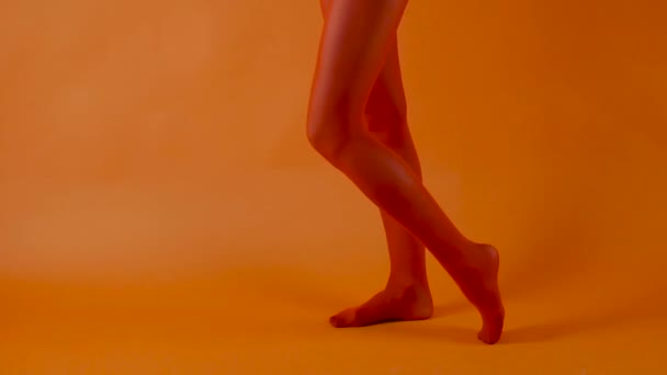 Czerwone pończochy na doskonałych kobiecych nogach na jasnym pomarańczowym tle, modelka tańczy w studio - Materiał filmowy, wideo