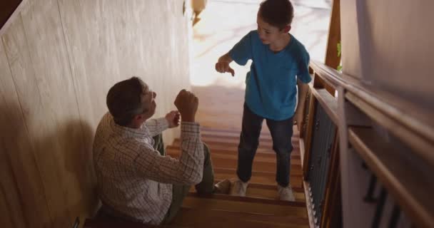 Vista de ángulo alto de un hombre caucásico y su hijo pequeño en casa, el padre sentado en las escaleras y el hijo de pie, que cinco altos, golpe de puño y abrazo, cámara lenta 4k
 - Metraje, vídeo