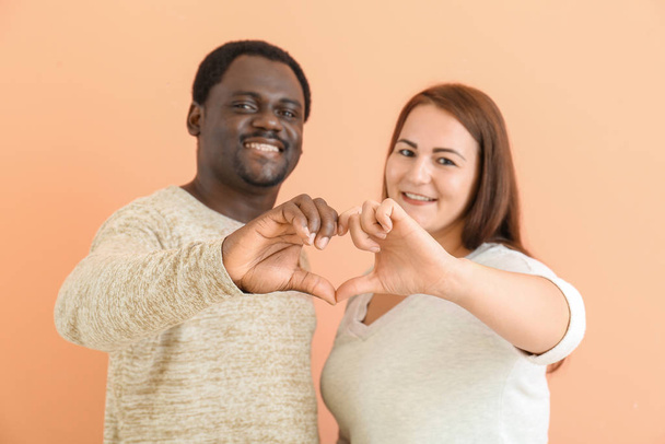 gelukkig interraciaal paar maken hart met hun handen op kleur achtergrond - Foto, afbeelding
