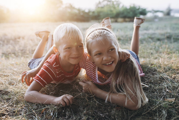 dvě blond děti, bratr a sestra objímající se na trávě - Fotografie, Obrázek