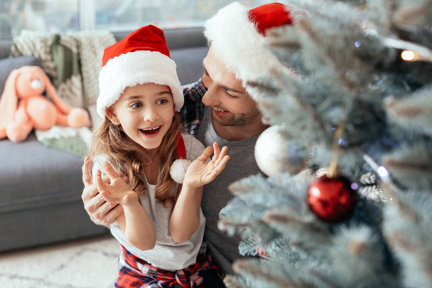 Dívka a její otec zdobí vánoční stromeček doma - Fotografie, Obrázek