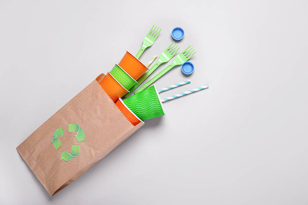Plastic cups, forks and paper bag on grey background. Recycling concept - Photo, Image