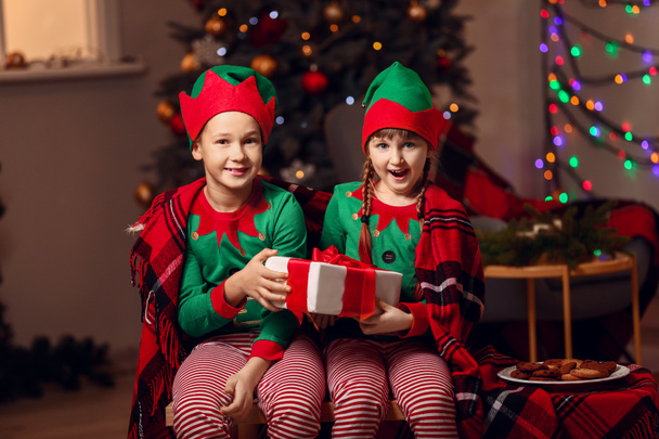 Bambini in costume da elfo e con regalo in camera decorato per Natale
 - Foto, immagini