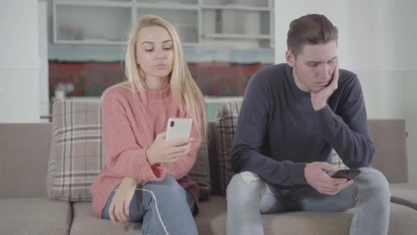 Portrait of young Caucasian woman and man sitting on sofa and using smartphones. Family members ignoring each other. Internet addiction, social media. - Filmagem, Vídeo