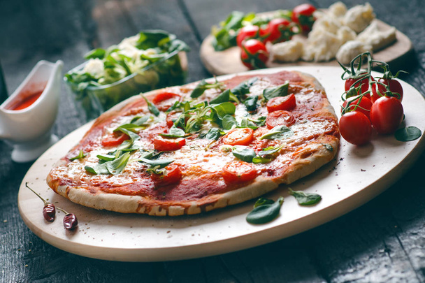 İtalyan yemeği, mutfak. Siyah ahşap bir masada Margherita pizzası. İçinde domates, salata, peynir, mozzarella, fesleğen gibi malzemeler var. Lezzetli ev yemekleri..  - Fotoğraf, Görsel