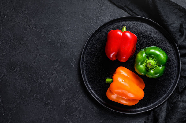 Green, orange and red bell peppers on a black plate. Black background. Top view. Space for text. - Photo, Image