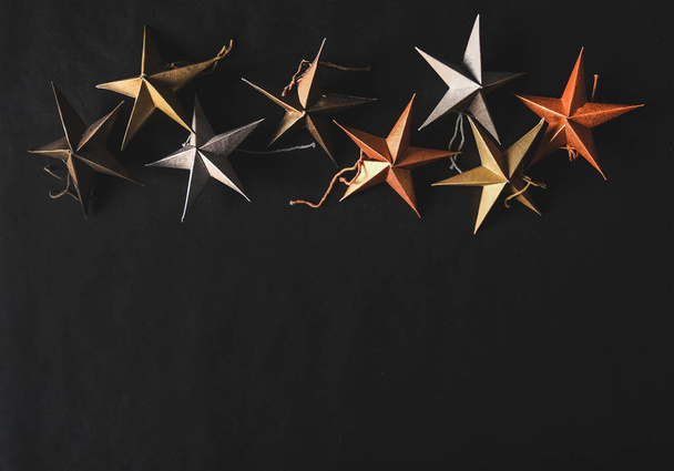 Christmas or New Year holiday texture, wallpaper and background. Flat-lay of paper toy decorative stars over black background, top view, copy space. Minimalistic concept - Fotó, kép