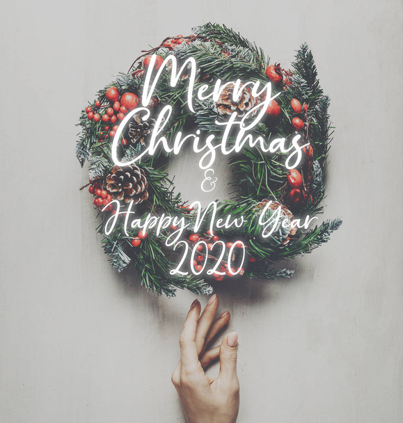 Home decoration for winter holidays. Female hand carefully touches a Christmas wreath on white background, wooden top view. New year concept - Foto, imagen