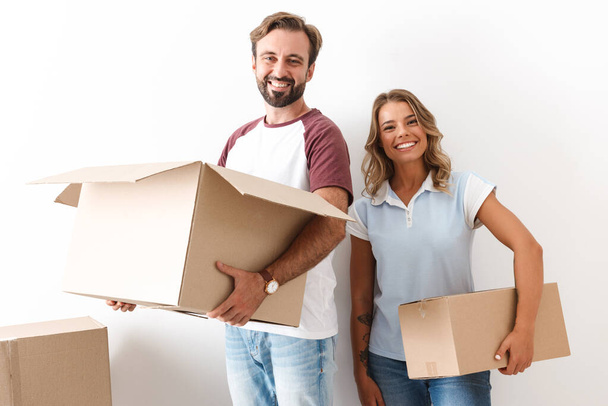 Photo of smiling couple ooking at camera and holding cardboard boxes - Photo, image
