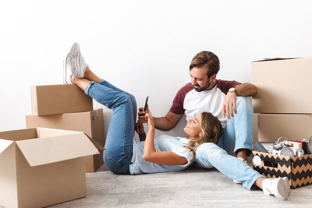 Photo of couple using cellphone while sitting near cardboard boxes - Photo, Image