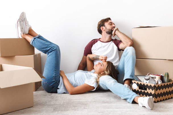 Photo of tired couple resting while sitting near cardboard boxes - Foto, Imagem